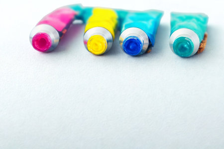 Four colorful tubes of paint, pink, yellow, blue, and teal, are arranged horizontally on a clean white background.の写真素材