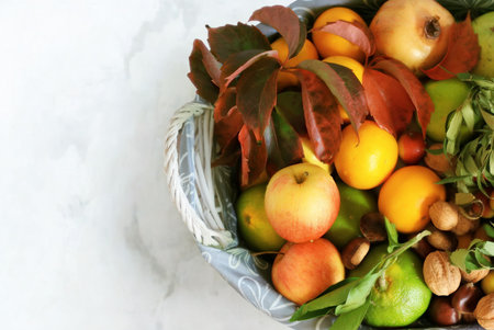 A close-up view of a basket overflowing with fresh fruits, nuts, and vibrant autumn leaves, showcasing a bountiful harvest.の写真素材