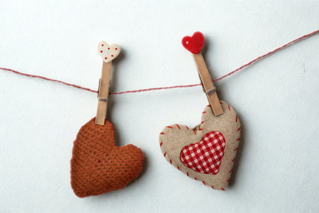 Two charming, rustic fabric heart ornaments, one brown and one with a red checkered pattern, hang suspended on a thin red string.の写真素材