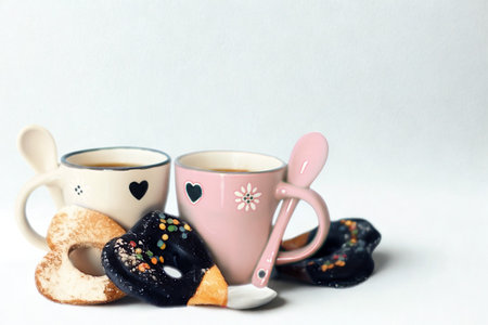 A still life composition featuring two decorative mugs, spoons, and assorted pastries against a plain background.の写真素材