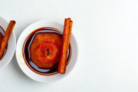 A close-up overhead view of a baked apple in a white dish, drizzled with dark syrup and topped with a cinnamon stick.の写真素材