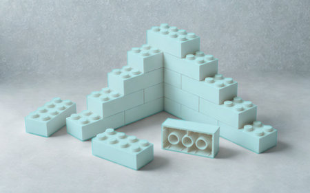 A pyramid-like structure of light blue building blocks, resembling a staircase, sits on a textured gray surface. Several loose blocks are scattered around.の写真素材