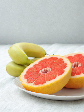 A close-up shot of two halves of a vibrant pink grapefruit and several green apples arranged on a white plate.の写真素材