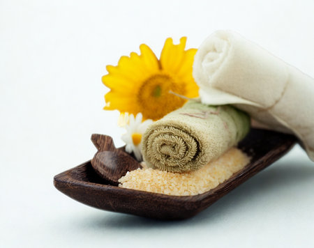 A serene spa arrangement featuring rolled towels, a bright yellow flower, and bath salts in a wooden dish.の写真素材