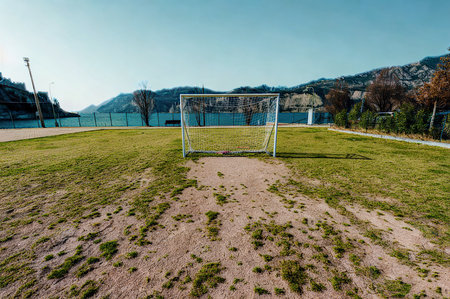 A wide-angle view of an empty soccer field. A goal stands at the far end, with grassy hills and trees behind it.の写真素材