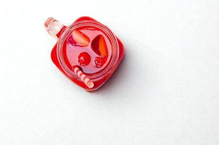 A close-up overhead view of a red heart-shaped glass jar filled with fruit jam and slices, casting a shadow on a white surface.の写真素材