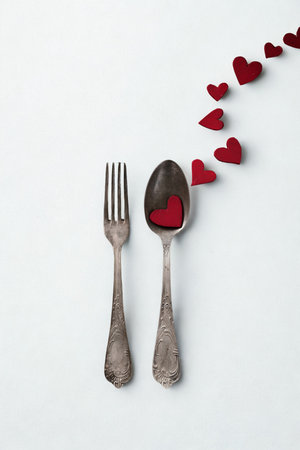A fork and spoon are placed on a white surface, with a trail of red heart shapes leading away from them.の写真素材
