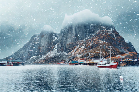 A serene winter scene in a Norwegian fjord with a red boat, snow-covered mountains, and falling snow.の写真素材