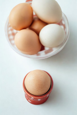 A collection of brown and white eggs are arranged in a bowl, with one brown egg prominently displayed in a small holder.の写真素材