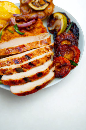 A close-up of a white plate filled with perfectly grilled, sliced chicken breast, accompanied by colorful roasted vegetables and lemon slices.の写真素材