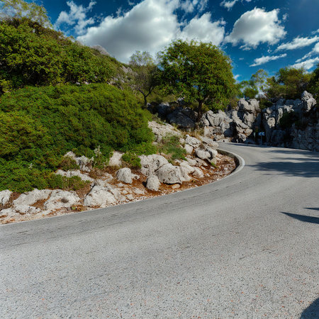 A winding road leads through a vibrant green landscape with scattered rocks and bushes under a sunny sky.の写真素材