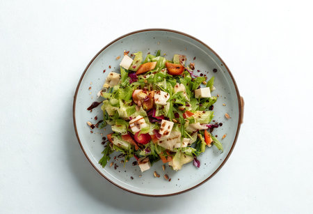 A top-down view of a colorful chopped salad featuring fresh greens, diced vegetables, feta cheese, and herbs, presented in a rustic bowl.の写真素材