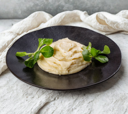 A close-up of fluffy mashed potatoes topped with vibrant green leaves, presented on a dark, textured plate.の写真素材
