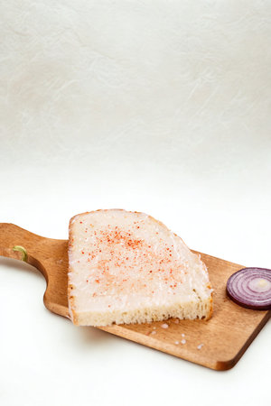 A close-up shot of a slice of bread seasoned with spices, placed on a wooden cutting board with a slice of red onion.の写真素材