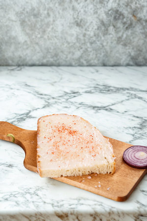 A close-up shot of a raw fish fillet seasoned with spices, placed on a wooden cutting board next to red onion slices.の写真素材