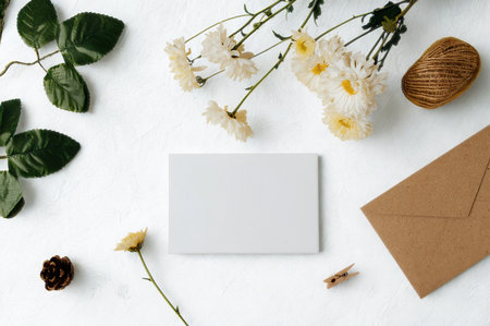 A flat lay composition featuring a blank card, brown envelope, delicate flowers, and natural elements on a white background.の写真素材