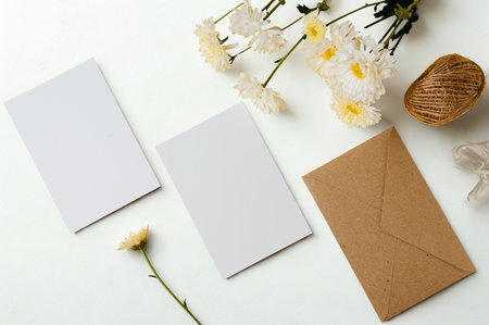 A flat lay composition featuring two blank white cards, a brown envelope, and dried flowers and greenery on a white surface.の写真素材