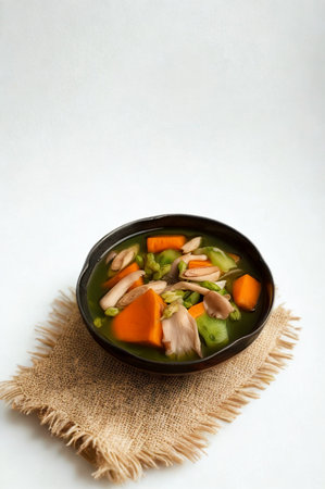A rustic bowl of steaming hot stew filled with colorful vegetables and chunks of meat sits on a textured burlap mat.の写真素材