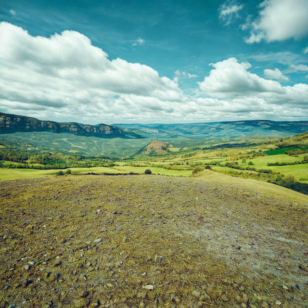 A vast landscape of green rolling hills stretches towards distant mountains under a dynamic sky filled with white clouds.の写真素材