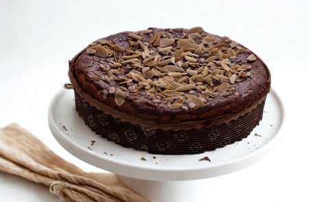A rich, dark chocolate cake is generously topped with chocolate shavings and presented on a classic white cake stand.の写真素材