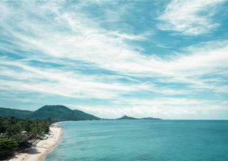 An idyllic tropical coastline with a white sand beach, clear turquoise water, and verdant,...
