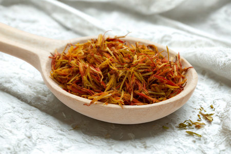 A close-up shot of dried saffron threads piled high in a light-colored wooden spoon, resting on a textured fabric surface.の写真素材