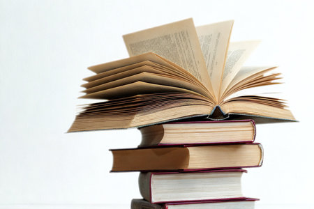 A tall stack of vintage books, with the top one dramatically opened, pages fanned out against a white background.の写真素材