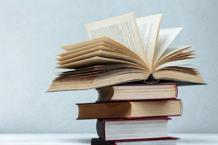 A pile of antique books, some open with pages fluttering, rests on a white surface against a soft blue background.の写真素材