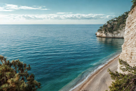 A tranquil beach with pebble shores meets the vibrant turquoise sea, framed by lush greenery and imposing rock formations under a bright sky.の写真素材