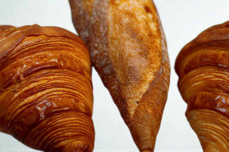 Close-up of three freshly baked pastries, two croissants and a baguette, showcasing their flaky texture and golden crust.の写真素材