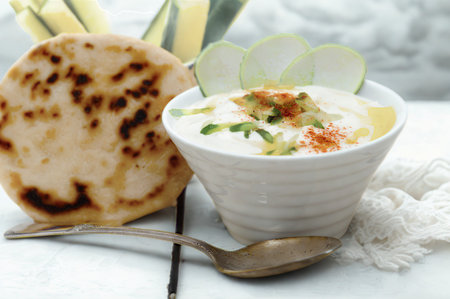 A creamy white yogurt dip topped with herbs and spices, served with a warm, fluffy flatbread and a spoon.の写真素材