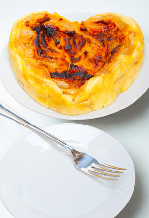 A heart-shaped baked dish with a golden brown crust sits on a white plate, with a fork resting on another plate below.の写真素材