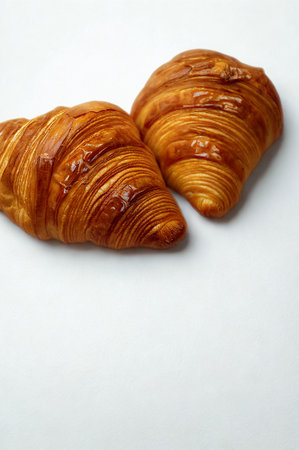 Two perfectly baked, flaky croissants with a rich golden brown crust sit side by side on a clean white surface.の写真素材
