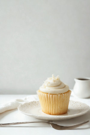 A single, golden-brown cupcake with swirls of white frosting sits on a white plate, ready to be enjoyed.の写真素材