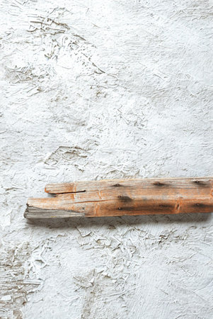 A single piece of weathered driftwood with a rough texture lies horizontally on a mottled, light-colored background.の写真素材