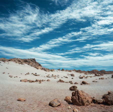 An expansive desert scene with sandy terrain, scattered rocks, and a vibrant blue sky filled with dynamic, wispy clouds.の写真素材