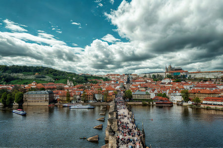 A bustling Charles Bridge in Prague, teeming with people, spans the Vltava River, leading to a picturesque cityscape under a dramatic sky.の写真素材