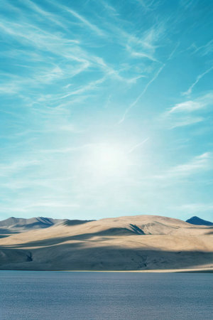 Expansive desert dunes stretch towards the horizon under a vibrant, cloud-streaked sky with a bright sun.の写真素材