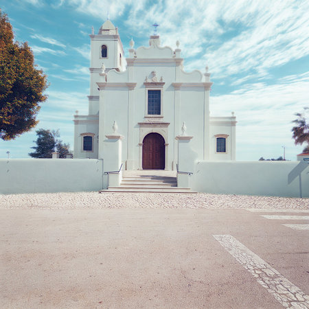 A bright white church with a prominent wooden door and steps, set against a vibrant blue sky with clouds.の写真素材