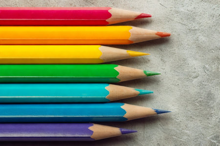 A close-up view of sharpened colored pencils arranged in a rainbow spectrum on a gray, textured background.の写真素材