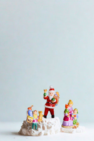 Small festive figurines of Santa Claus and a group of children are arranged on a white surface against a light blue background.の写真素材