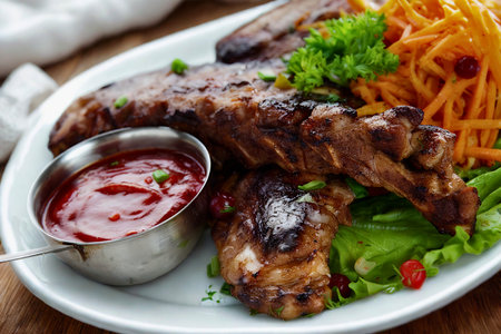 A close-up shot of succulent grilled ribs served with a refreshing salad and a small metal cup of dipping sauce.の写真素材