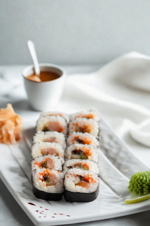 A close-up of several delicious sushi rolls arranged on a white platter, served with a small bowl of dipping sauce and fresh garnishes.の写真素材