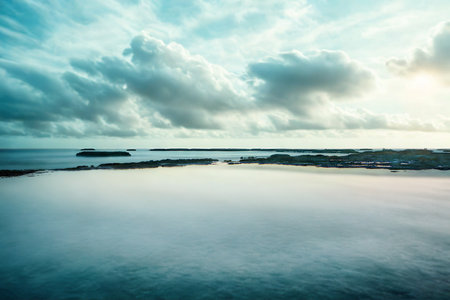 A serene ocean stretches to the horizon, reflecting a dramatic sky filled with teal and white clouds, hinting at approaching weather.の写真素材