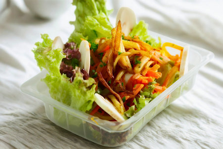 A close-up view of a colorful salad with lettuce, vegetables, and dressing, presented in a transparent container.の写真素材