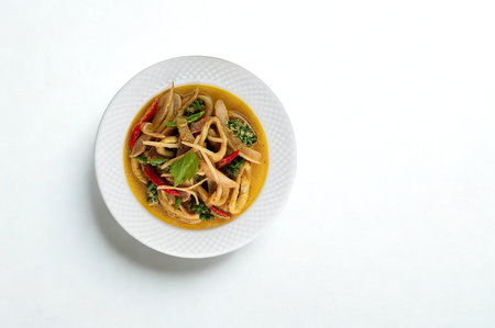 A top-down view of a white plate filled with a vibrant Thai basil stir fry featuring squid, vegetables, and a savory sauce.の写真素材