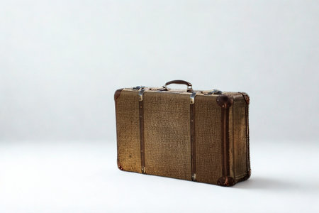 A single, aged brown suitcase with a textured surface sits on a clean white surface, casting a subtle shadow.の写真素材