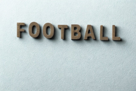 Three-dimensional wooden letters spelling "FOOTBALL" are casting shadows on a plain, light-colored surface.の写真素材