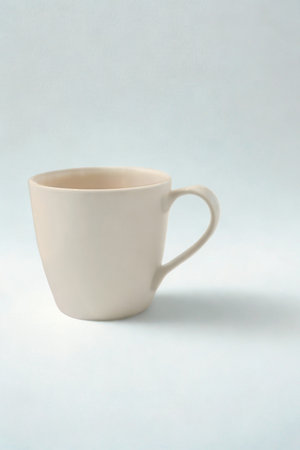 A single, light-colored ceramic mug with a textured exterior sits on a white surface, casting a subtle shadow.の写真素材