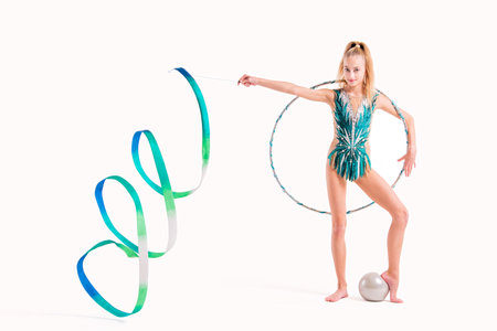 Smiling girl professional gymnast in an emerald swimsuit poses with a ribbon, hoop and ball isolated on a white backgroundの写真素材